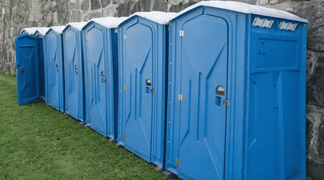 Row of blue portable toilets lined up on grass against a stone wall for event sanitation in Erie, PA