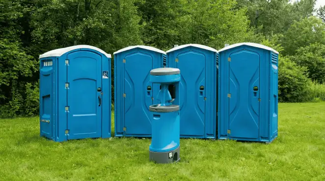 Four blue portable toilets and a matching hand washing station on grass near trees, a common sight at local outdoor events in Erie, PA