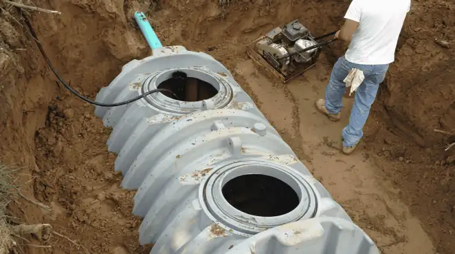 Septic tank installation showing a technician compacting soil around a new poly septic tank in an excavation pit in Erie, PA